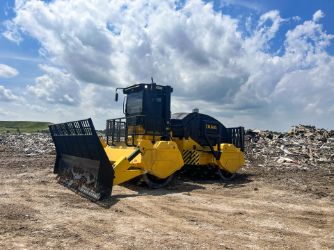 Image of the TANA H555eco at a landfill site. Image is of front left of the machine. There is a landfill behind the machine.